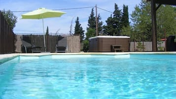 Ein klares Schwimmbecken mit Holzterrasse, ein überdachter Whirlpool und ein eingezäunter Bereich mit Sitzgelegenheiten.