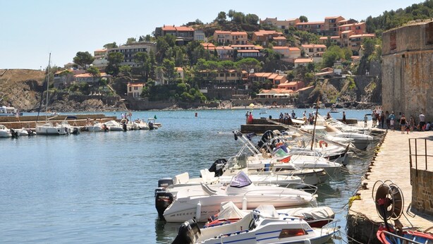 Un port de plaisance où des bateaux sont amarrés le long de la rive, entouré d’une colline parsemée de bâtiments.