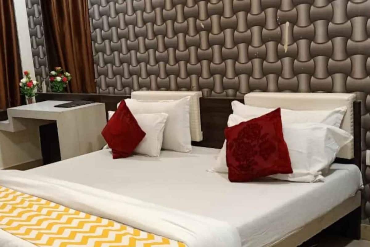 Een hotelkamer met een modern design, met een groot bed met witte beddengoed en rode kussens, een klein nachtkastje en een decoratieve hoofdbord.