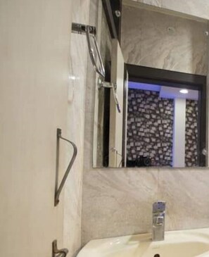 Ein Badezimmer mit Marmorwand, Waschbecken mit Wasserhahn und Spiegel mit verzierter Rahmen.