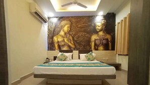 A bedroom with a large bed, a ceiling fan, a decorative wall with a Buddha statue, and a patterned rug. - Hotel Maa Ganga palace (Bhopal)