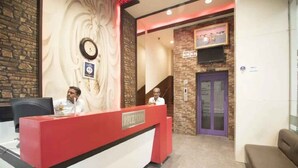 A reception area with a red desk, a clock, and a staircase leading to an elevator. - Hotel Maa Ganga palace (Bhopal)
