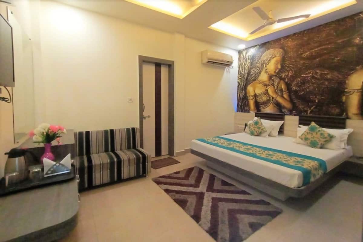 Een hotelkamer met een bed, een bank, een bureau met een computer en een muurschildering.