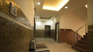A hotel hallway with a bench, a staircase, and a reception area. - Hotel Maa Ganga palace (Bhopal)