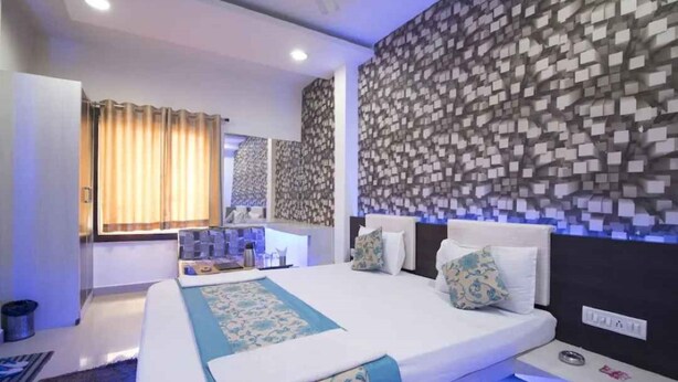 A modern hotel room with a large bed, a bedside table, a mirror, and a patterned wall. - Hotel Maa Ganga palace (Bhopal)