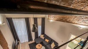 Een moderne woonkamer met een bank, salontafel en hanglampen. Een trap leidt naar een hoger gelegen verdieping.