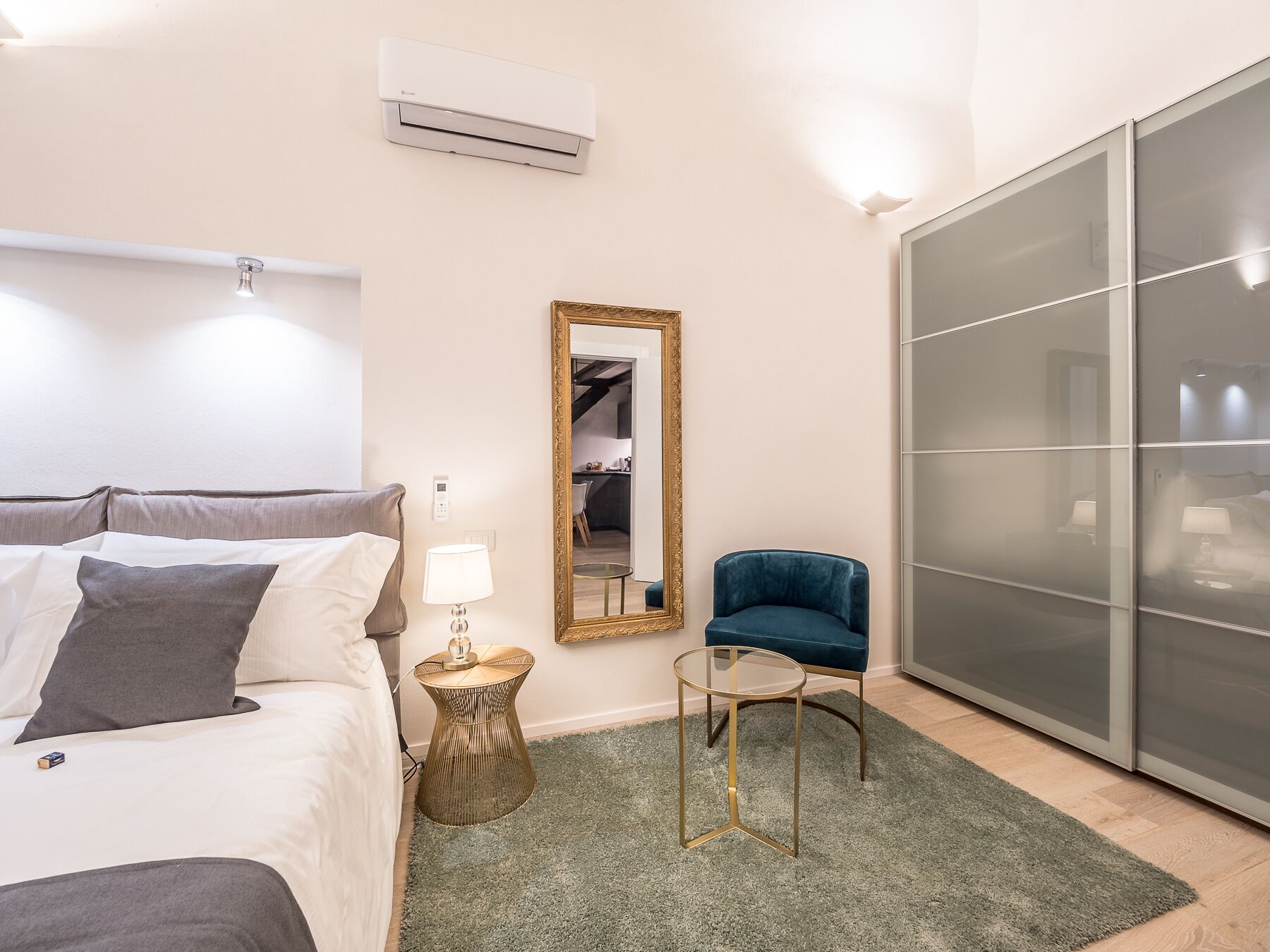 A bedroom with a bed, bedside lamp, mirror, chair, and wardrobe.