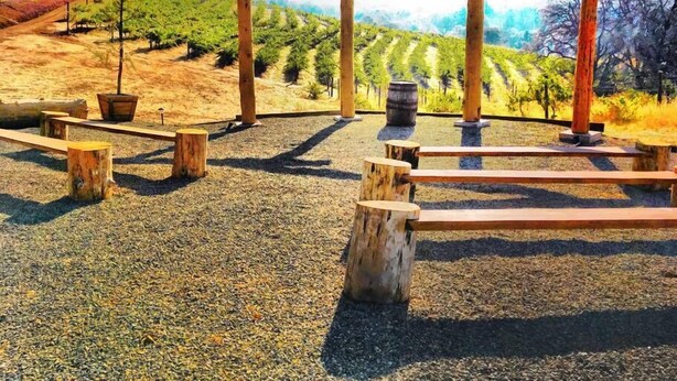 A wooden pergola structure with benches in a vineyard setting. - Papillon Cellars (Mariposa)
