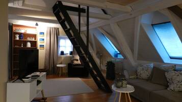 A loft-style room with a slanted ceiling, a built-in desk, a sofa, and a ladder.