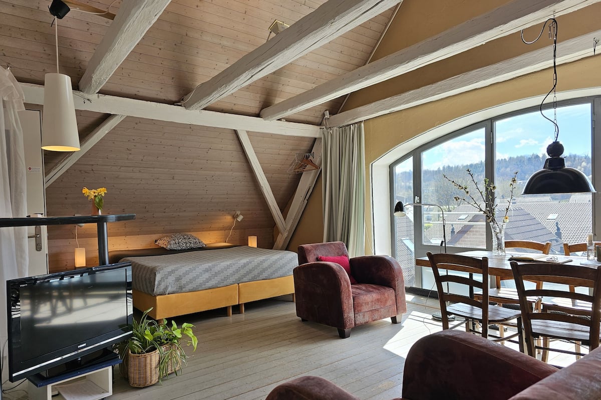 Een gezellige kamer met een bed, een televisie, een eettafel en een groot raam met uitzicht.