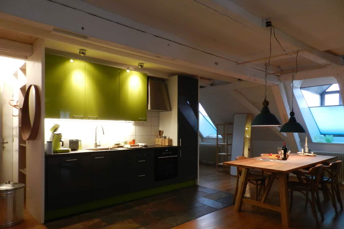 Een moderne keuken met groene kasten, een houten eettafel en een dakraam.