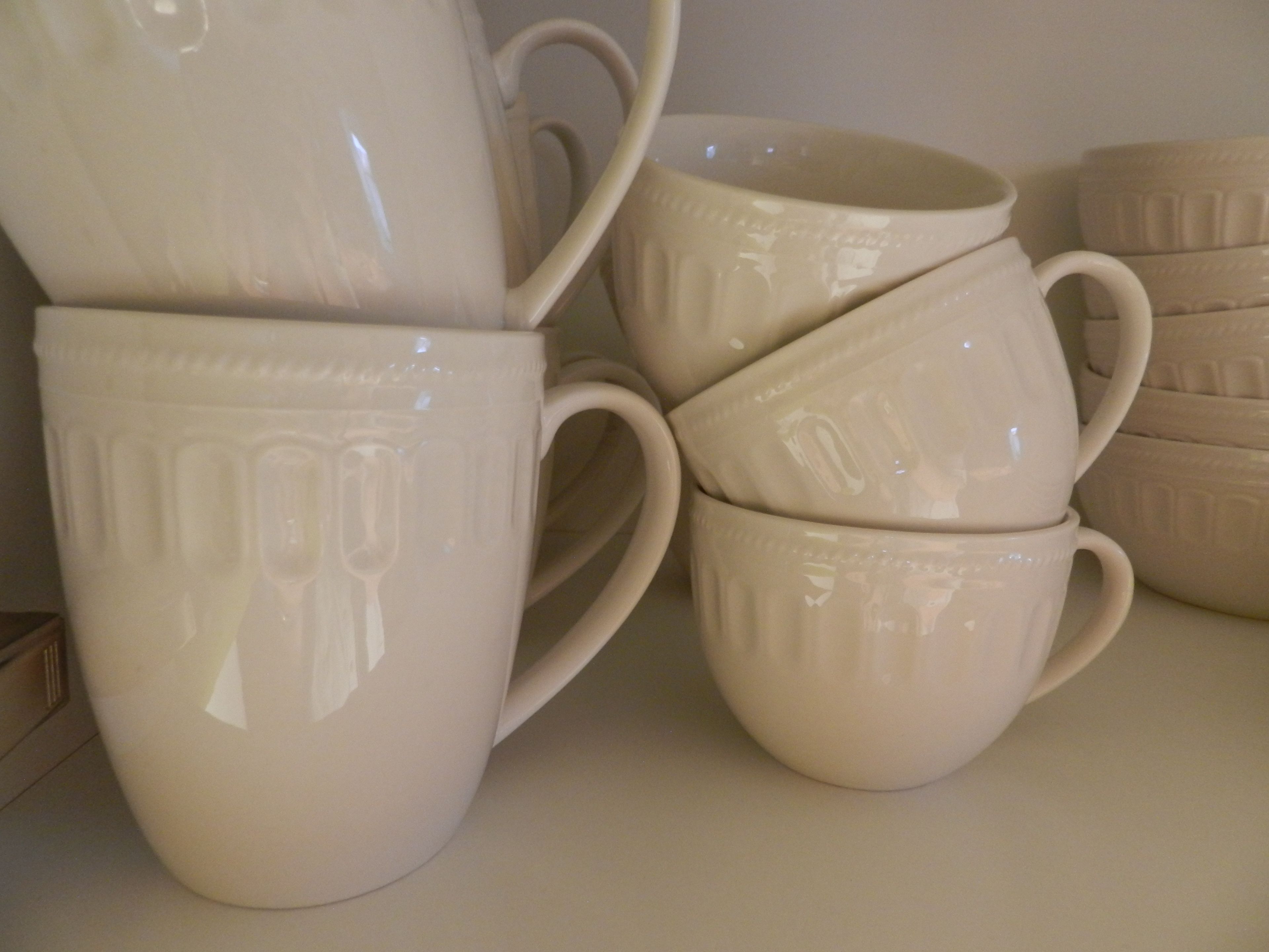 Une pile de tasses en céramique blanche, ornées de motifs en relief, posée sur une surface plane.