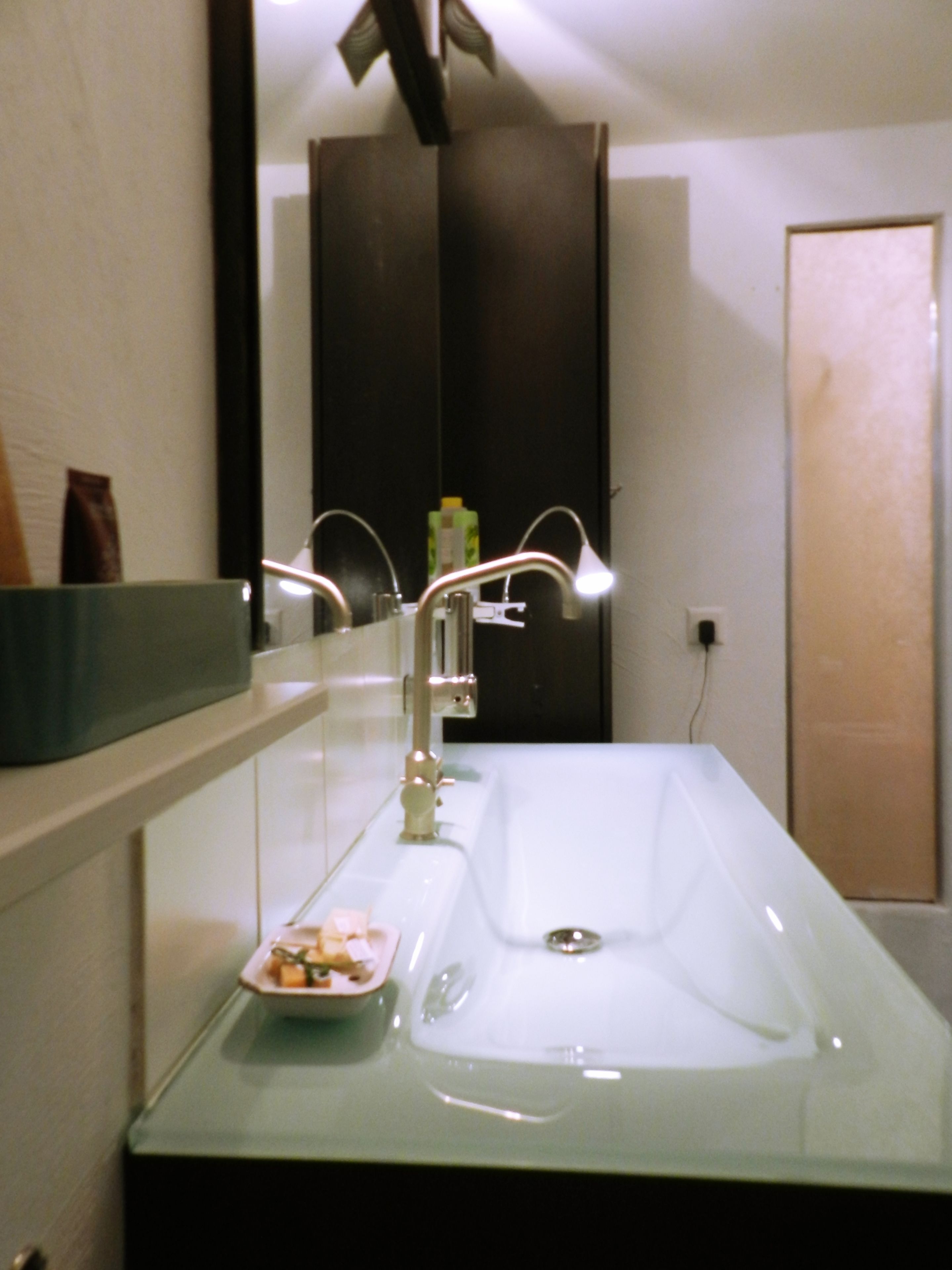 A bathroom with a glass-enclosed sink, a mirror, and a towel rack.