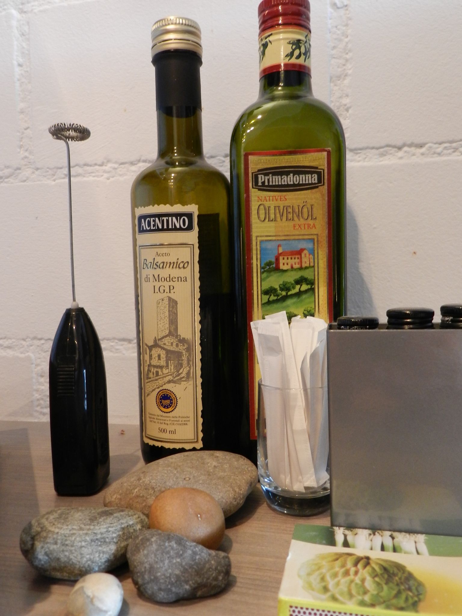Deux bouteilles d’huile d’olive, un petit objet noir et quelques pierres sur une surface en bois.