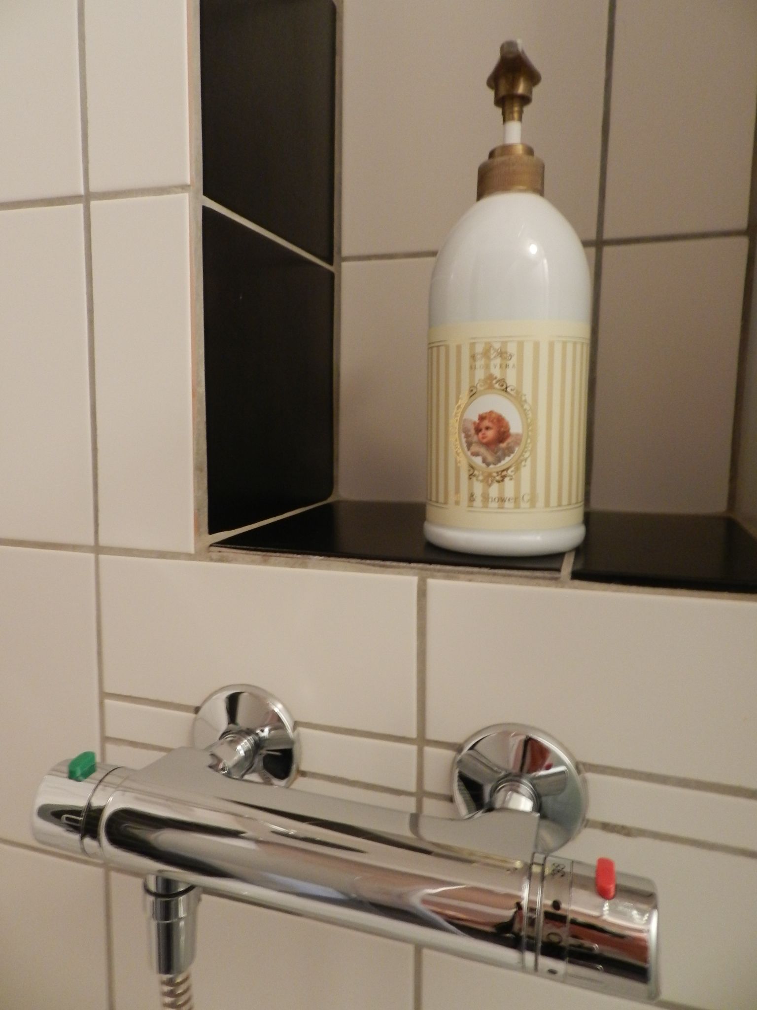 A bathroom with a white tiled wall, a chrome faucet, and a soap dispenser on a shelf.