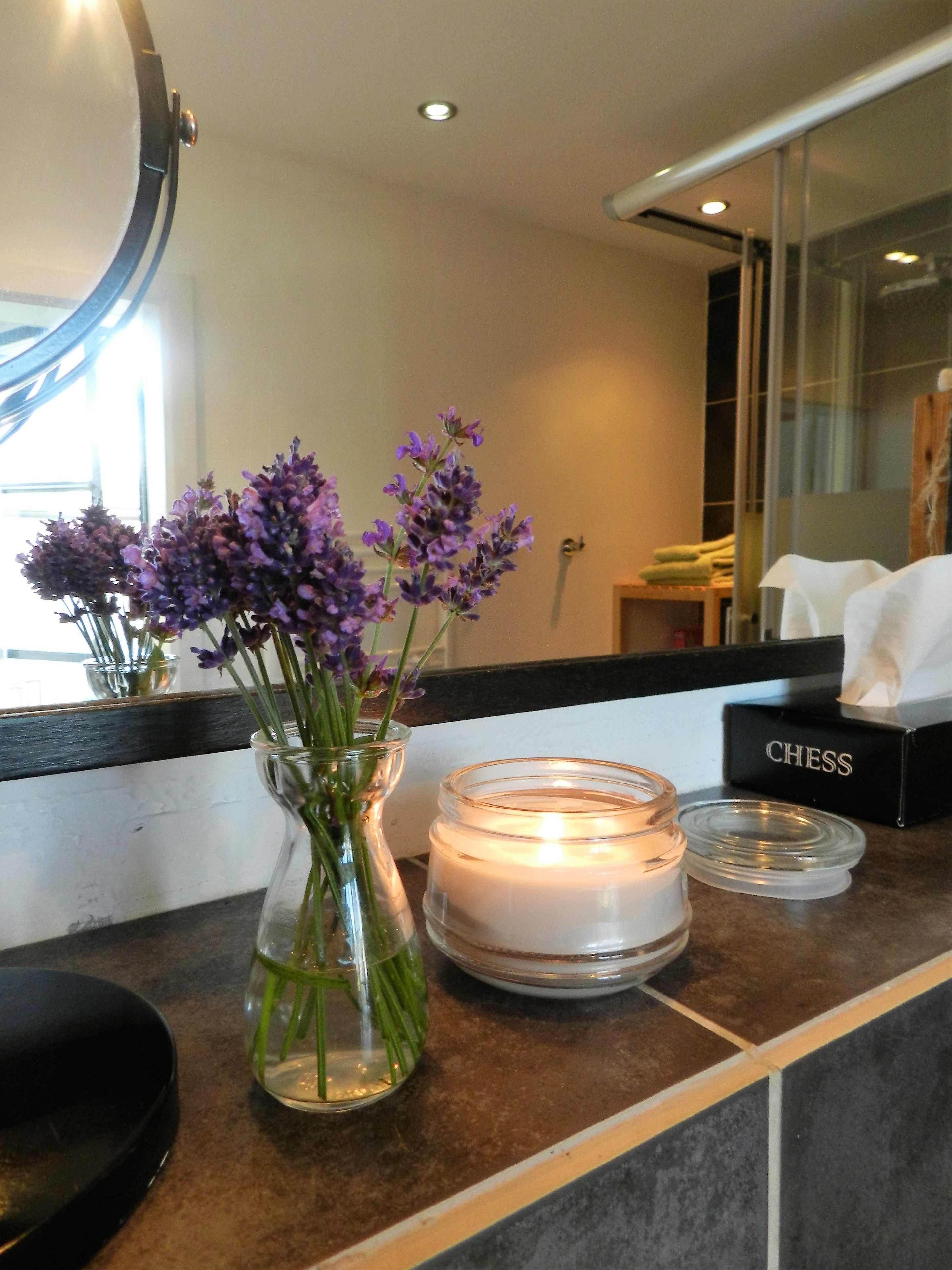 Ein Zimmer mit einer Anrichte, auf der eine Vase mit violetten Blumen, eine brennende Kerze und ein Schachspiel stehen.