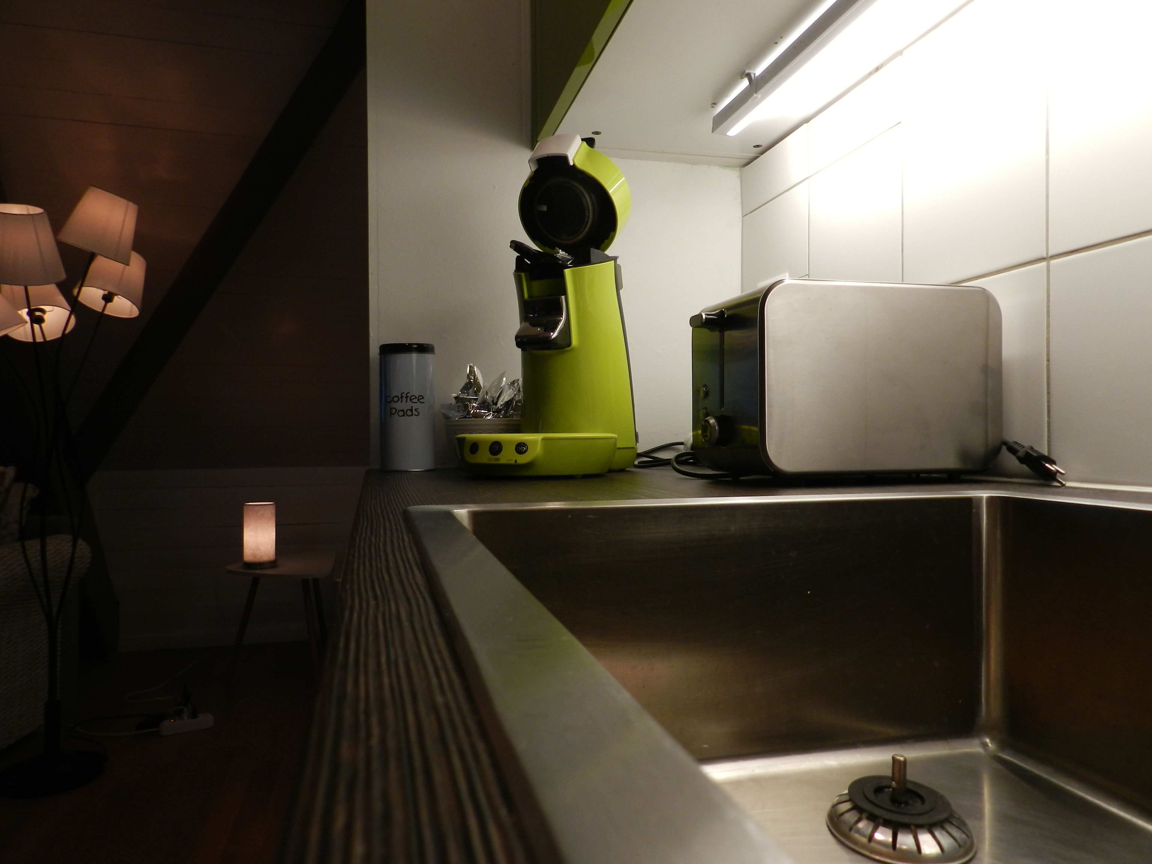 Una cocina moderna con un lavamanos de acero inoxidable, una cafetera verde y un tostador blanco.