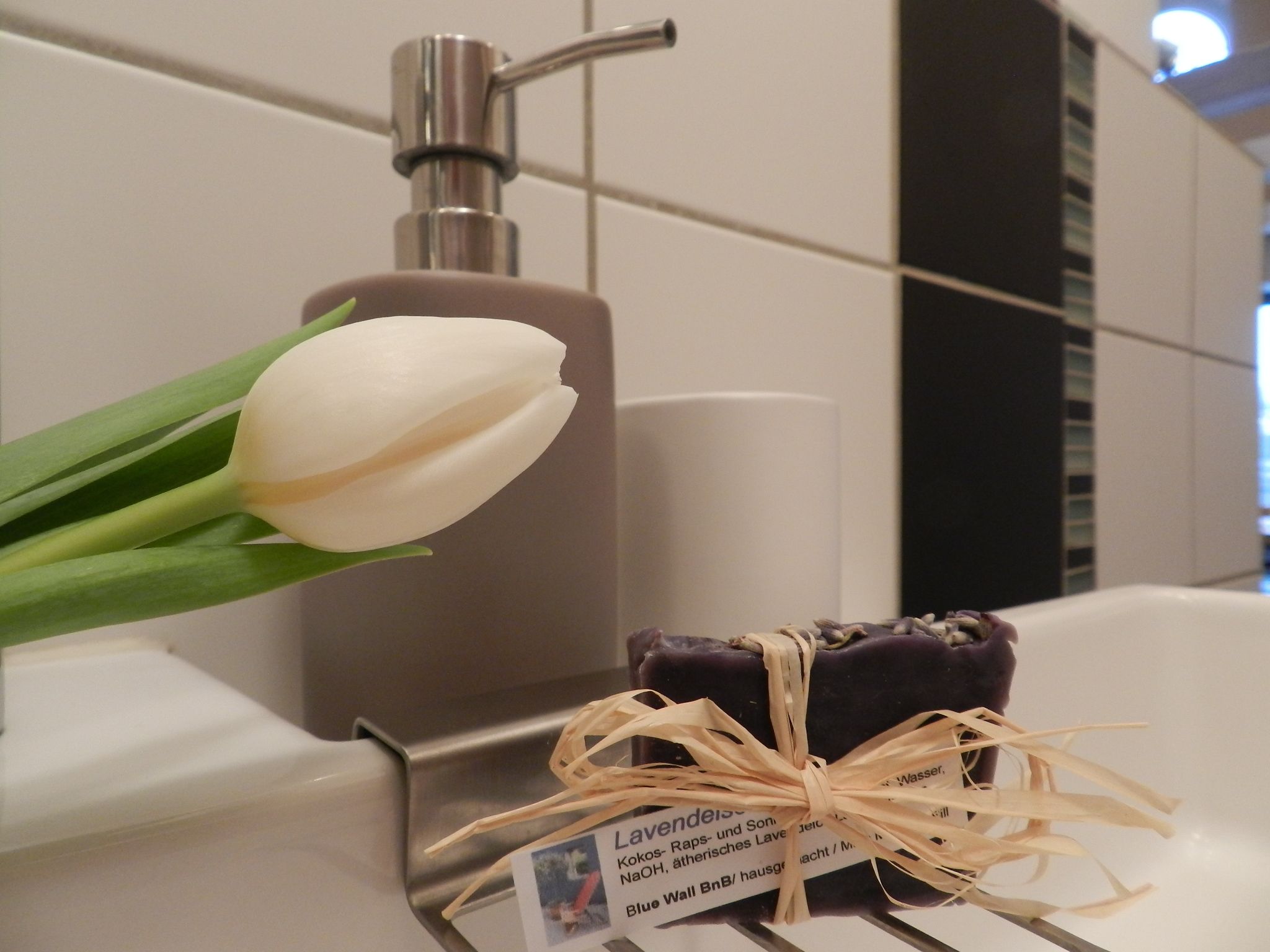 A bathroom with a white sink, a bottle of soap, and a bouquet of white tulips.