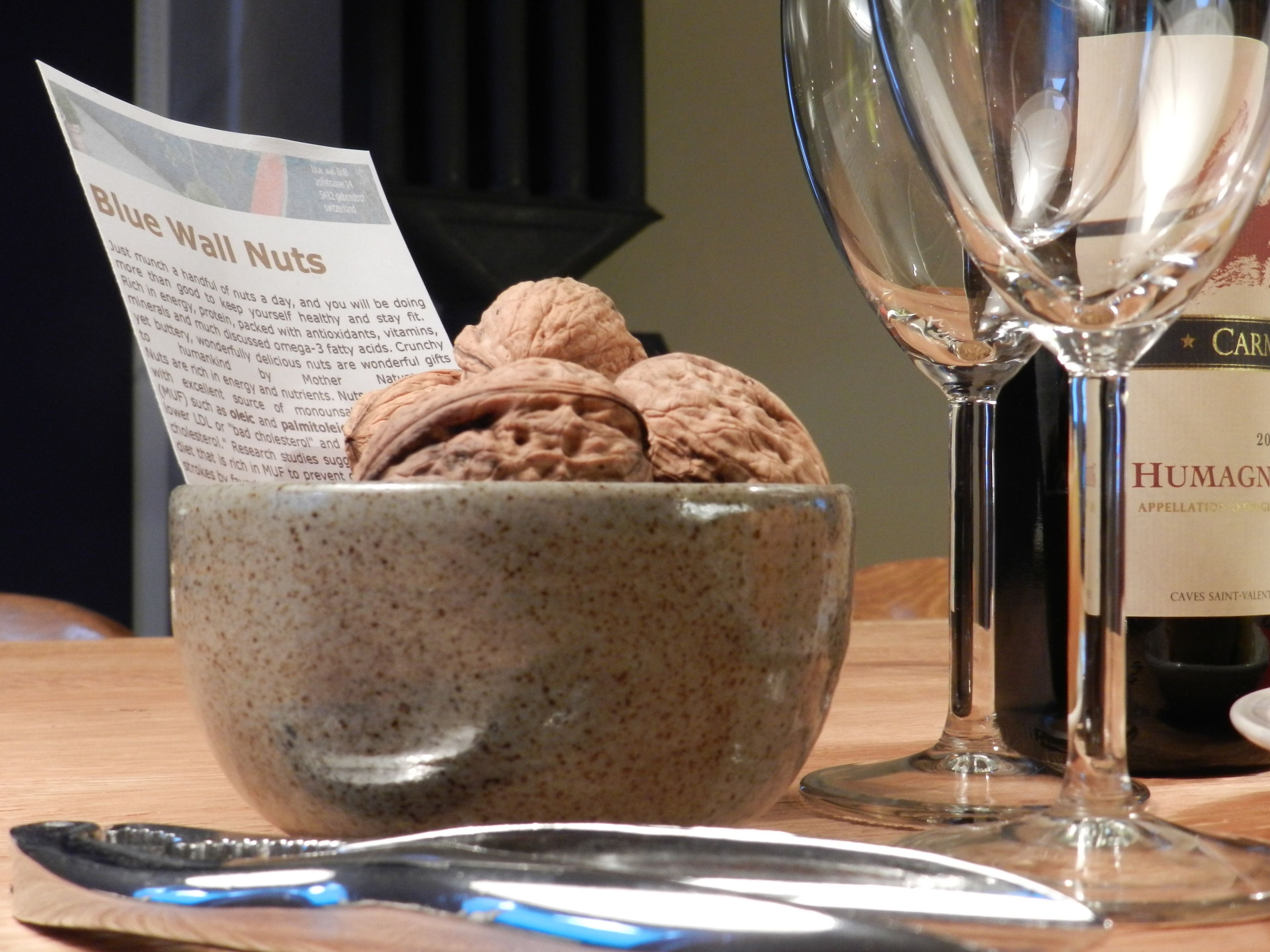 A bowl of nuts, a wine glass, and a bottle of wine on a table.