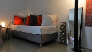 A bedroom with a bed, pillows, a bedside table, a lamp, a mirror, and a wall-mounted light fixture.