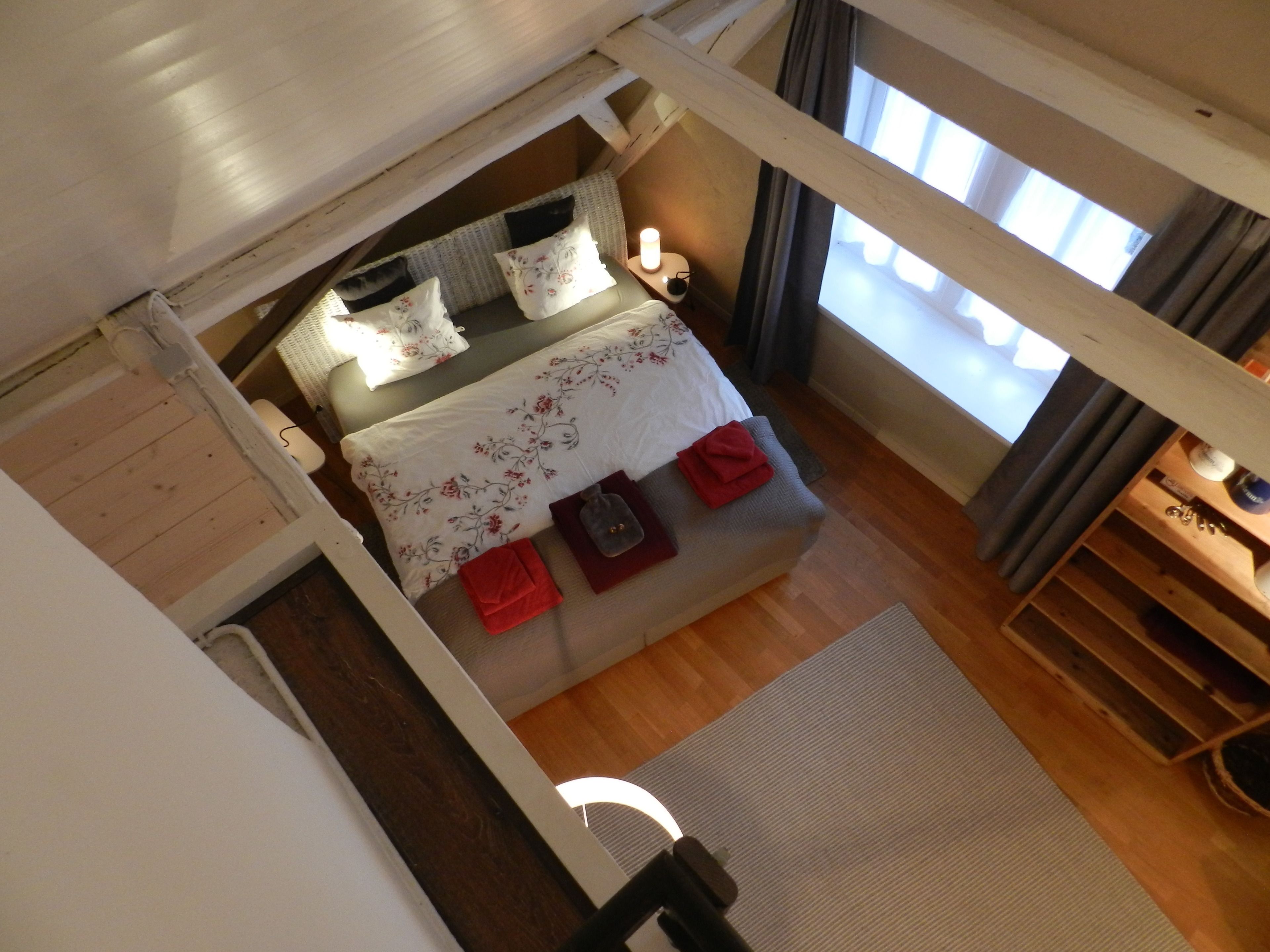 Un dormitorio con cama, almohadas, mesita de noche y ventana con cortinas.