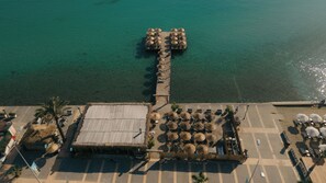 An aerial view of a beachside resort with a central pier, beach umbrellas, and lounge chairs. - Nars Ilica Hotel Beach (Cesme)