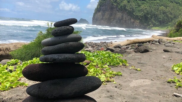 A stack of smooth, rounded stones on a beach with a view of the ocean and a cliff in the background.
