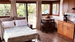 A bedroom with a large bed, a wooden ceiling, a dining area with a table and chairs, and a kitchen with wooden cabinets.