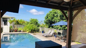 A backyard with a swimming pool, lounge chairs, and a covered patio area.