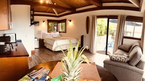 A compact room with a bed, a small desk with a coffee maker, a sofa, and a view of the outdoors through a sliding door.