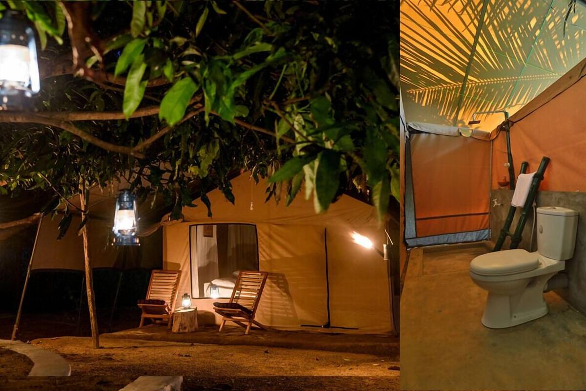 A tent with a single bed, a chair, and a small table. There is a toilet and a lamp outside the tent.