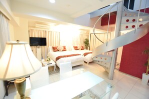 A hotel room with a bed, a desk, a chair, a lamp, a TV, and a spiral staircase.