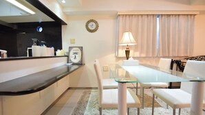 A modern kitchen with a glass dining table and white chairs, a clock on the wall, and a window with curtains. - Mell-Theater 1102 (Osaka)