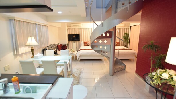 A modern hotel room with a dining area, a bed with a red accent wall, a staircase, and a TV. - Mell-Theater 1102 (Osaka)