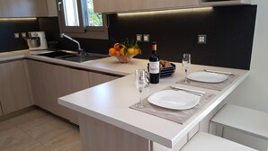 Una cucina moderna con isola centrale, forno integrato e lavello. Sull'isola, due piatti bianchi, una bottiglia di vino e un bicchiere.