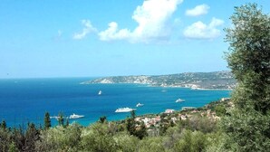 Vista costiera con barche, cielo sereno e un paesaggio collinare con edifici.