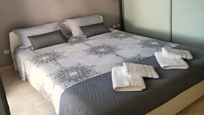 Un letto ben rifatto con copripiumino a fantasia, due cuscini e asciugamani piegati sulla testiera.