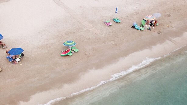 Vista aerea di una spiaggia con diversi ombrelloni, lettini e persone che si rilassano.