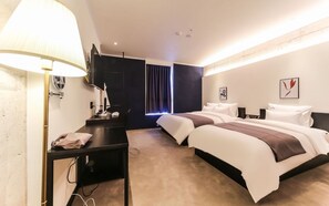 Habitación de hotel con dos camas, un escritorio, un televisor y obras de arte en las paredes.
