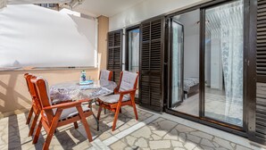 Un balcón con una mesa y sillas, una botella de agua y vista al interior a través de una puerta de cristal.