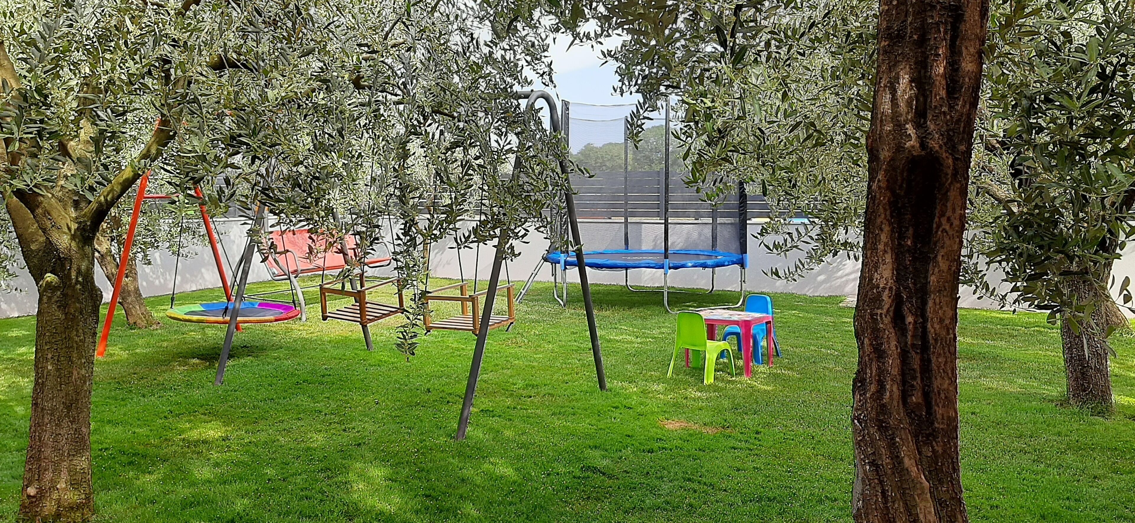 Un'area giochi con altalene, un trampolino e sedie colorate.