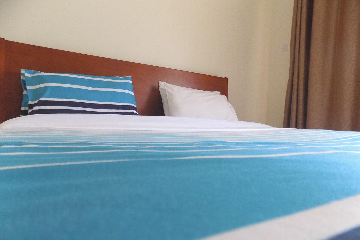 Una cama con colcha azul y blanca a rayas, un almohadón blanco y un cabecero marrón.