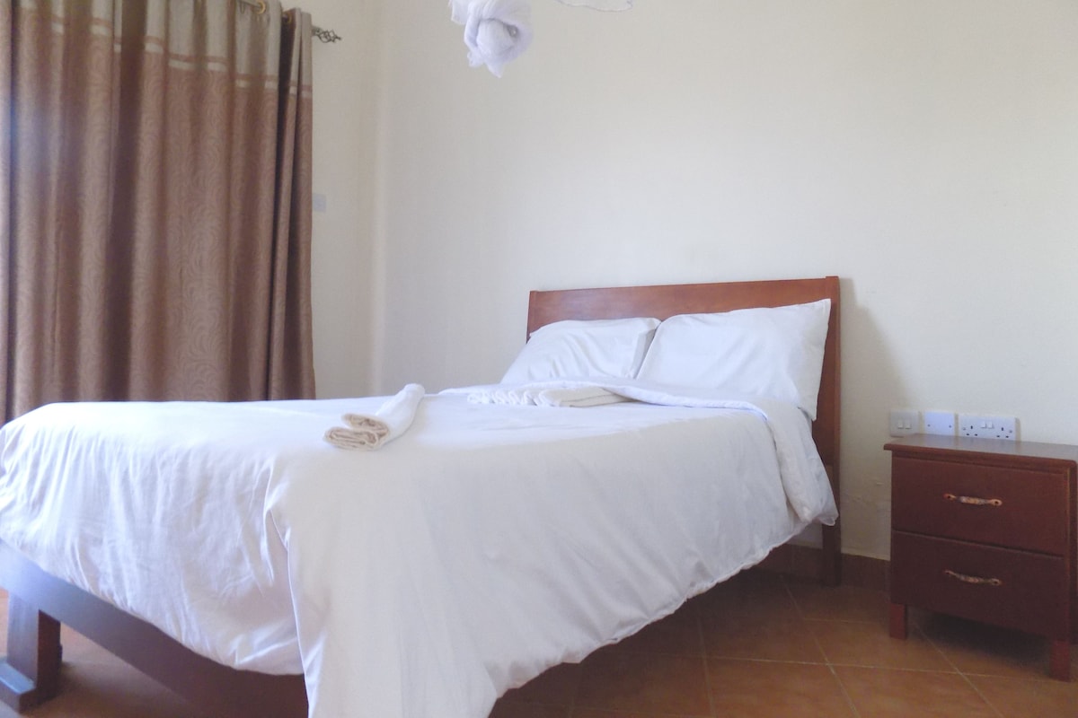 Una cama bien hecha con sábanas blancas, cabecera de madera y una mesita de noche con cajones.