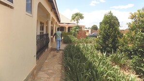 A covered walkway with a stone floor leading to a building with a tiled roof. - Plain Springs Hotel (Kumi)