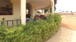A covered outdoor seating area with tables and chairs, surrounded by greenery. - Plain Springs Hotel (Kumi)