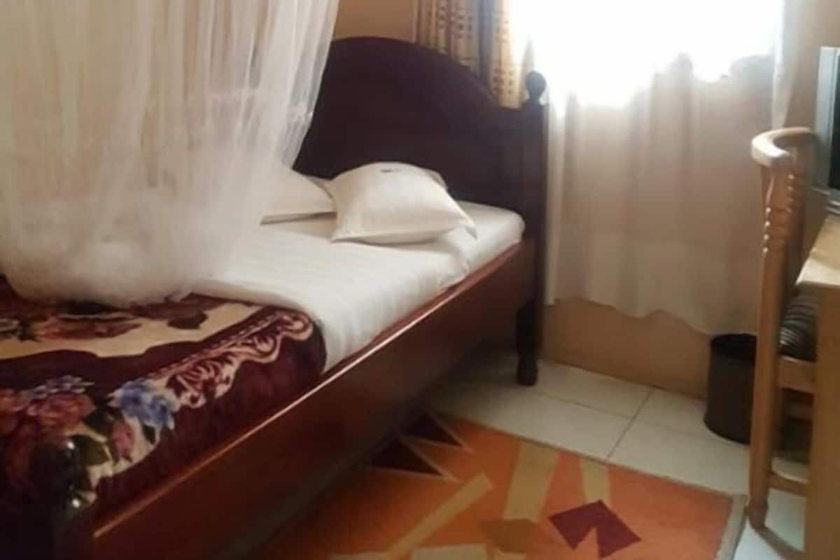 Una cama con dosel, una silla, una ventana con cortinas y una alfombra estampada.
