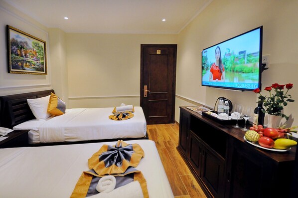 Habitación de hotel con dos camas, un televisor, un escritorio con una bandeja de frutas y un cuadro en la pared.