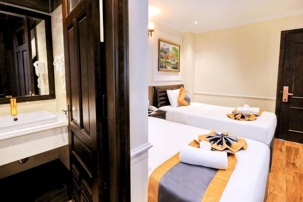 A hotel room with a wooden door, a white sink, two beds with towels, a painting on the wall, and a wooden floor.