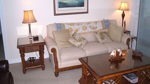 Sala de estar com sofá, duas mesas laterais com luminárias, uma mesa de centro e um quadro pendurado na parede.