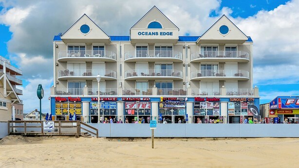 Um hotel na praia com várias varandas e diversos estabelecimentos comerciais no andar térreo.